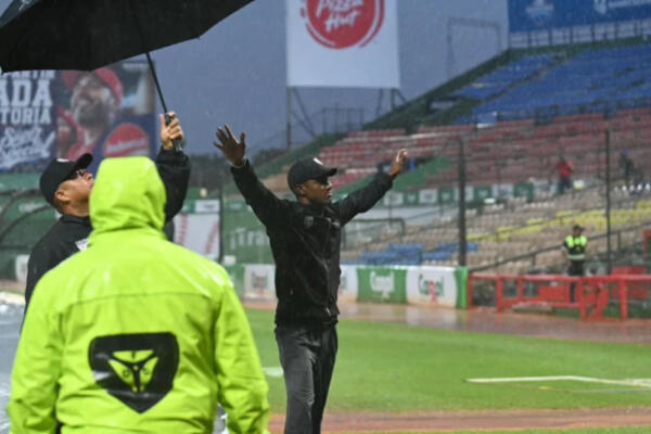 El arbitro principal Yunior Torres, levanta sus brazos para indicar que el juego fue pospuesto por lluvia