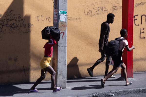 Fotografía de tres personas caminando con sus pertenencias en Puerto Príncipe (Haiti). EFE