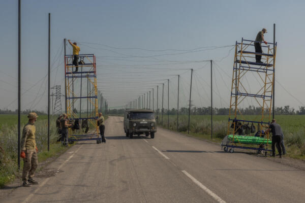 A car drives past Ukrainian servicemen installing anti-drone nets over a road at an undisclosed location in the eastern Donetsk region on July 8, 2025, amid the Russian invasion of Ukraine. (Photo by Roman PILIPEY / AFP)