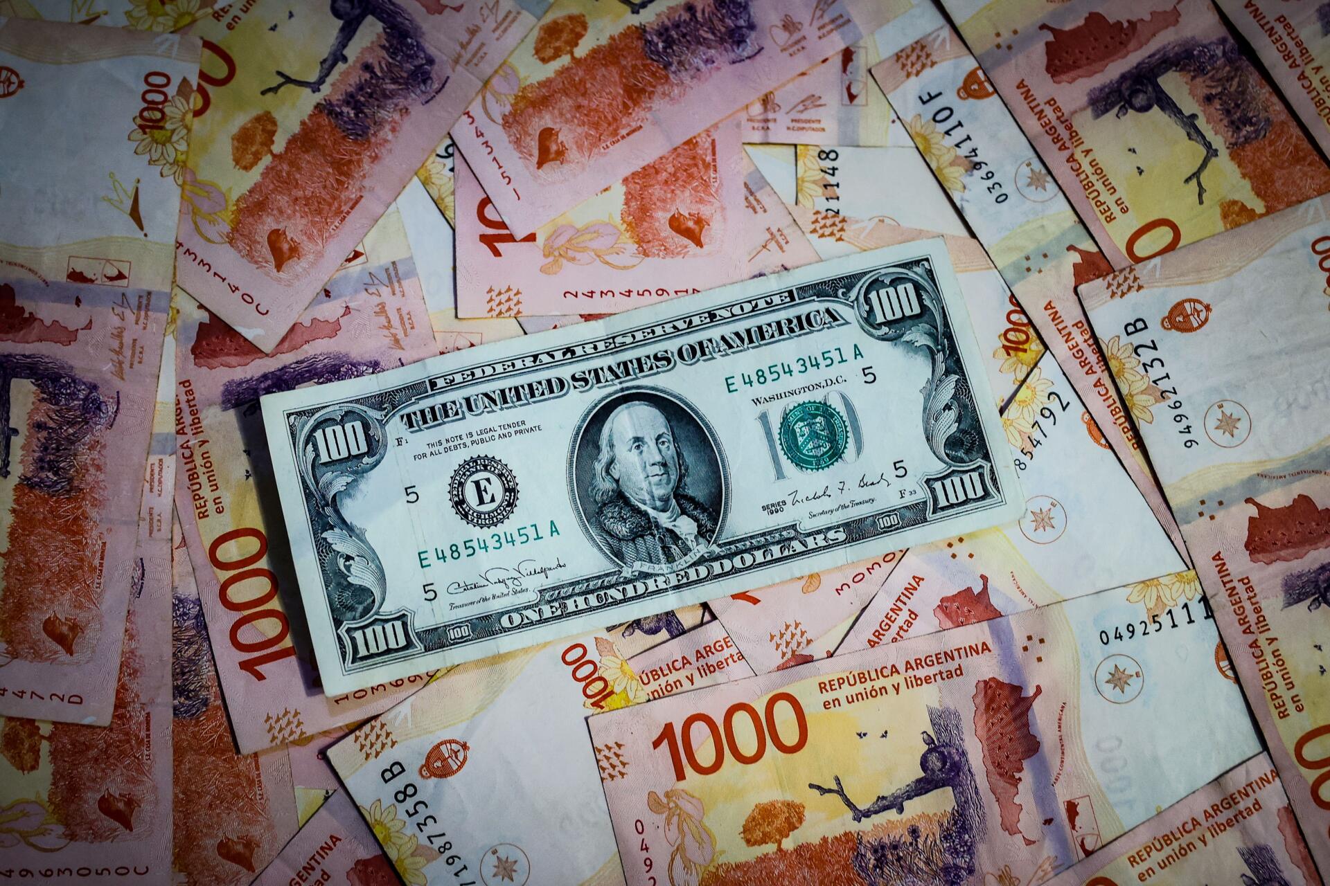 Fotografía de archivo comparativa de billetes de pesos argentinos con un billete de 100 dolares estadounidenses
