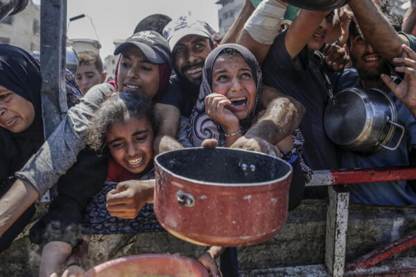 Palestinos desplazados internos, incluidos niños, sostienen ollas mientras se reúnen para recibir alimentos de un comedor benéfico en Gaza. EFE/Mohammed Saber
