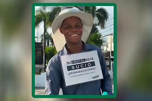 Joven limpia vidrios en Santo Domingo con letrero ofreciendo su servicio