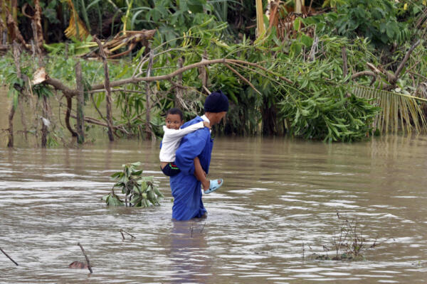 Fotografía del 29 de octubre de 2025 de un hombre cruzando un río crecido mientras carga a un niño, en el poblado de Guama en Santiago de Cuba (Cuba). EFE/ Ernesto Mastrascusa