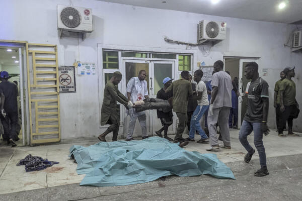 Varias personas trasladan a un hombre herido entre cuerpos cubiertos con sábanas en un hospital de Maiduguri el 16 de marzo de 2026, tras las explosiones ocurridas en la ciudad.  (FOTO: AFP). 