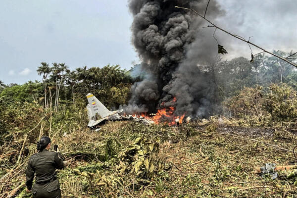 Llamas y una densa columna de humo negro se elevan desde un avión Hércules de la Fuerza Aérea que se estrelló durante el despegue, mientras un miembro de la Policía colombiana permanece cerca, en Puerto Leguizamo, Colombia, cerca de la frontera sur con Ecuador, el 23 de marzo de 2026. El ejército colombiano informó el 23 de marzo que se creía que unos 80 soldados habían muerto tras el accidente de un avión de transporte en el sur del país. (Foto de Daniel Ortiz / AFP)
