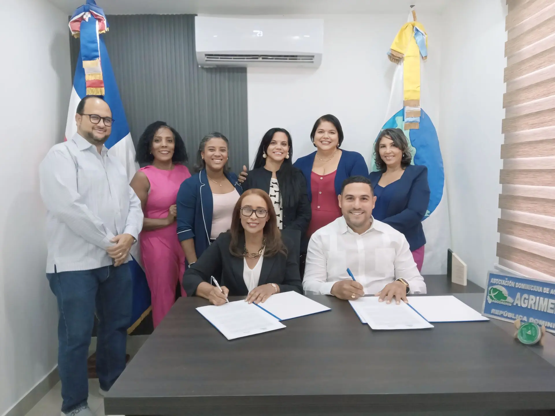 Erminda Decena y Victor Torres firman el convenio. Miembros de las juntas directivas de las entidades les acompañan.