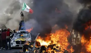 Manifestante sostiene una bandera mexicana junto a coches en llamas en Los Ángeles, el 8 de junio de 2025.