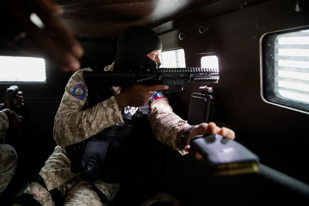 Un agente de policía haitiano apunta con su arma por la ventana de un vehículo blindado durante una patrulla en el centro de Puerto Príncipe el 16 de enero de 2026.